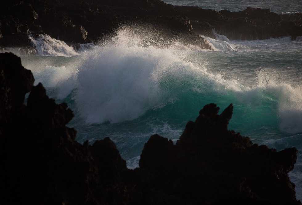 A view of a strong wave crashing into rocks along the Hawaii coastline.